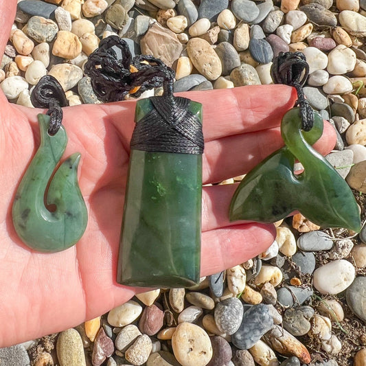 Authentic New Zealand Greenstone pendants including a toki, hook and whale tail held in hand, representing meaningful New Zealand gifts for Kiwis living in Australia.