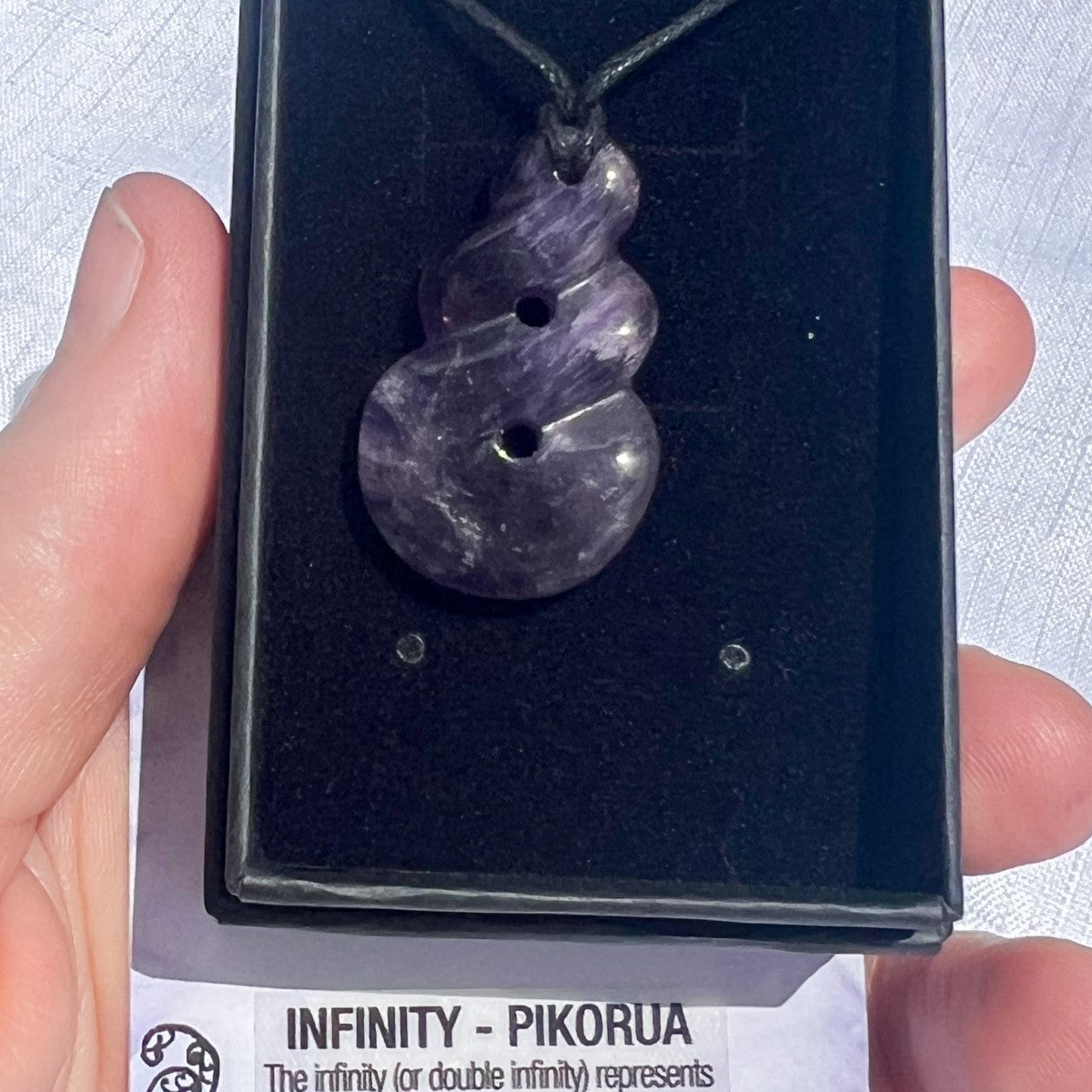 Purple stone pendant on a black card held by a hand