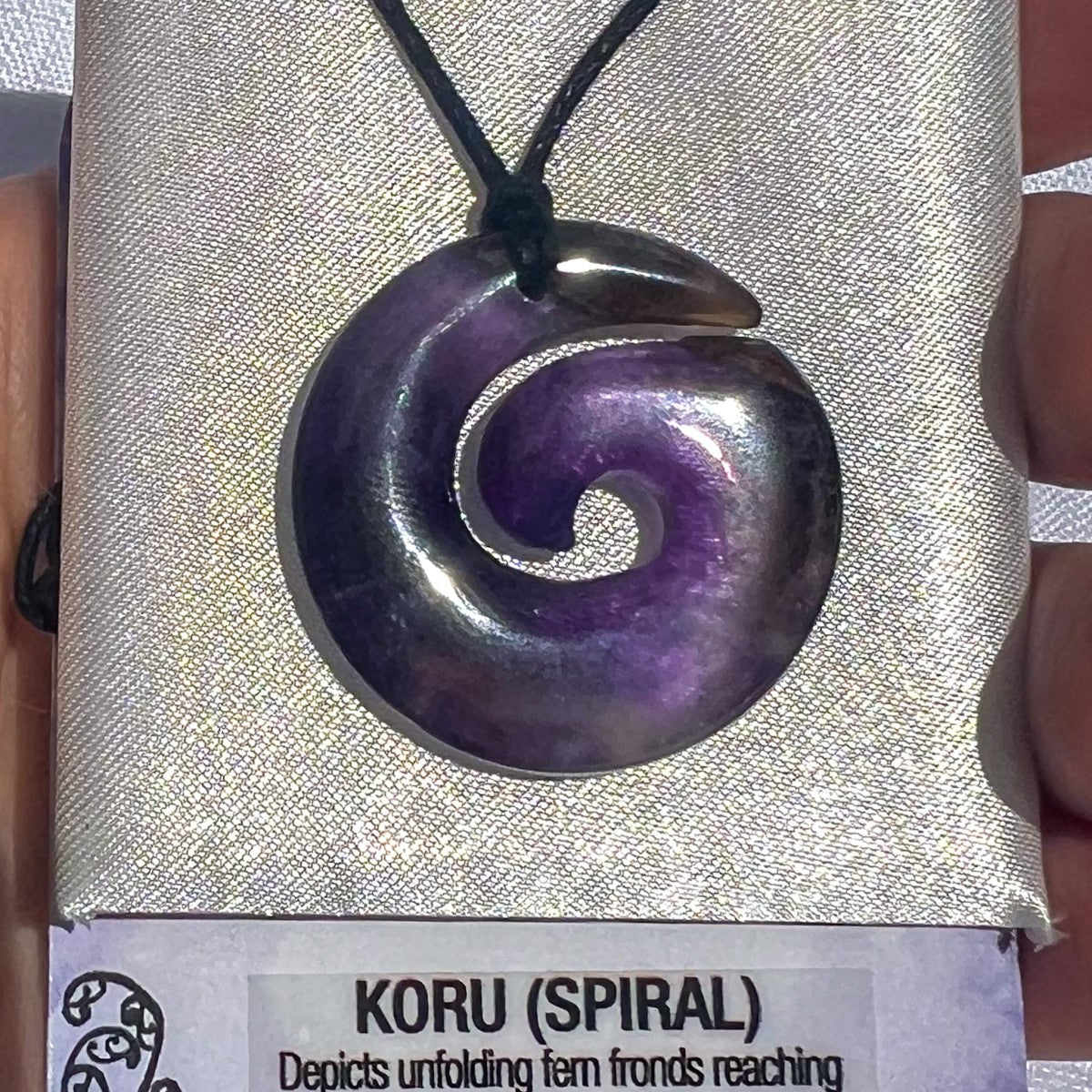 Purple koru spiral pendant on a black cord against a gray fabric background