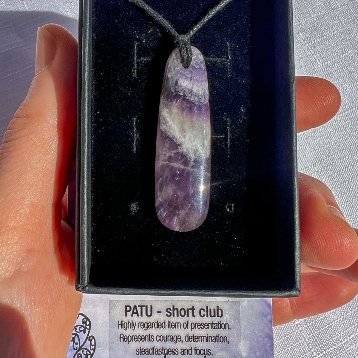 Amethyst pendant necklace held by a hand with a label below.