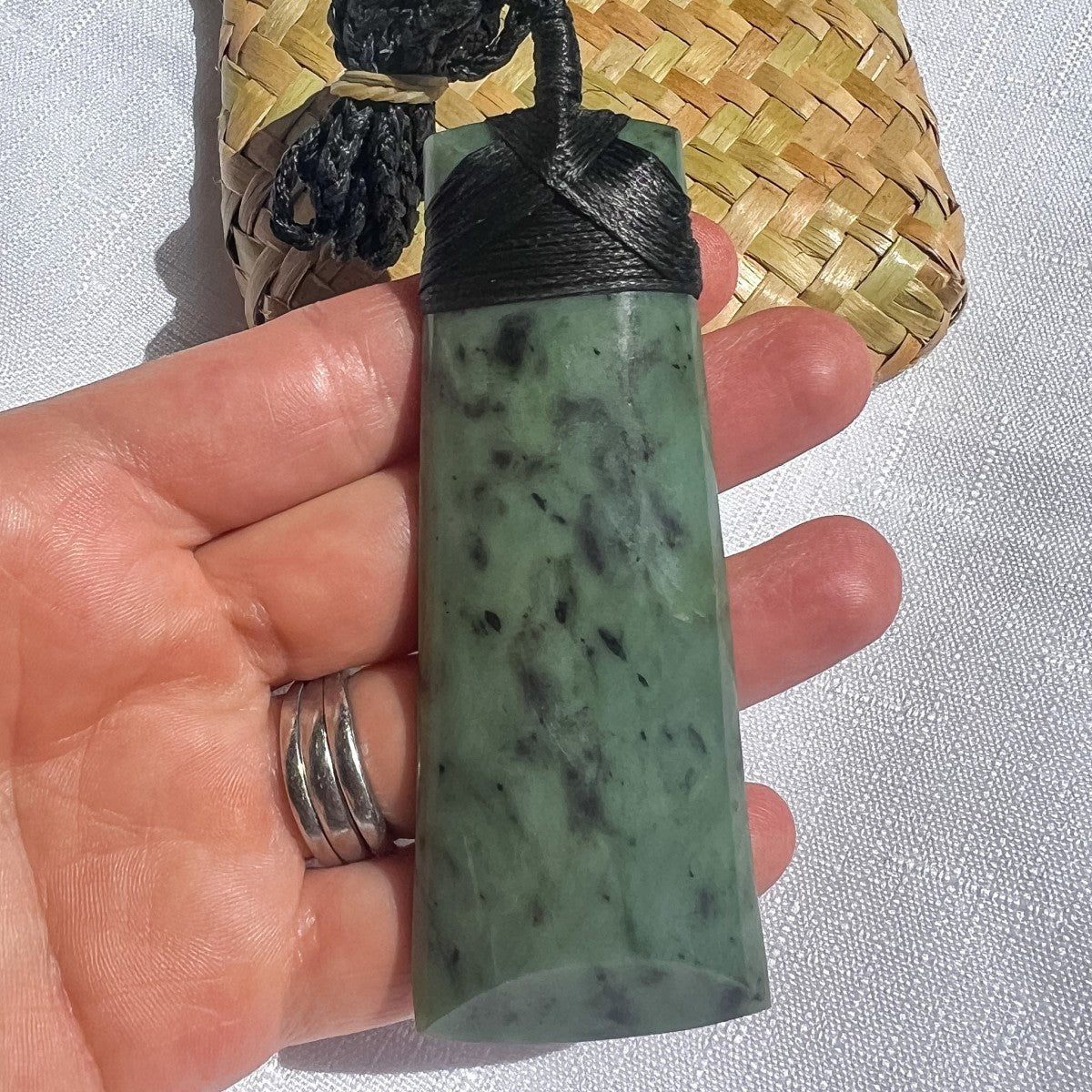 NZ Greenstone pendant with black cord held in a hand against a light background