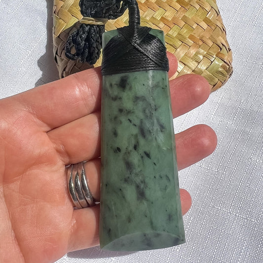 NZ Greenstone pendant with black cord held in a hand against a light background