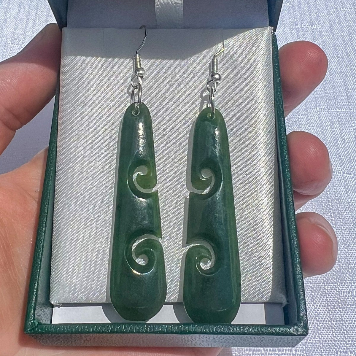 Green jade earrings with silver hooks displayed in a jewelry box.