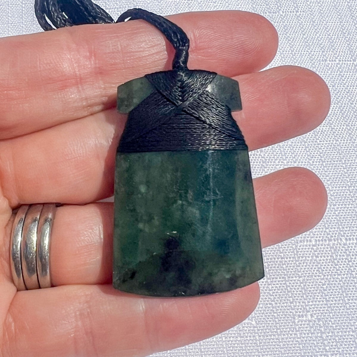 Green stone pendant on black cord held between fingers with a white background