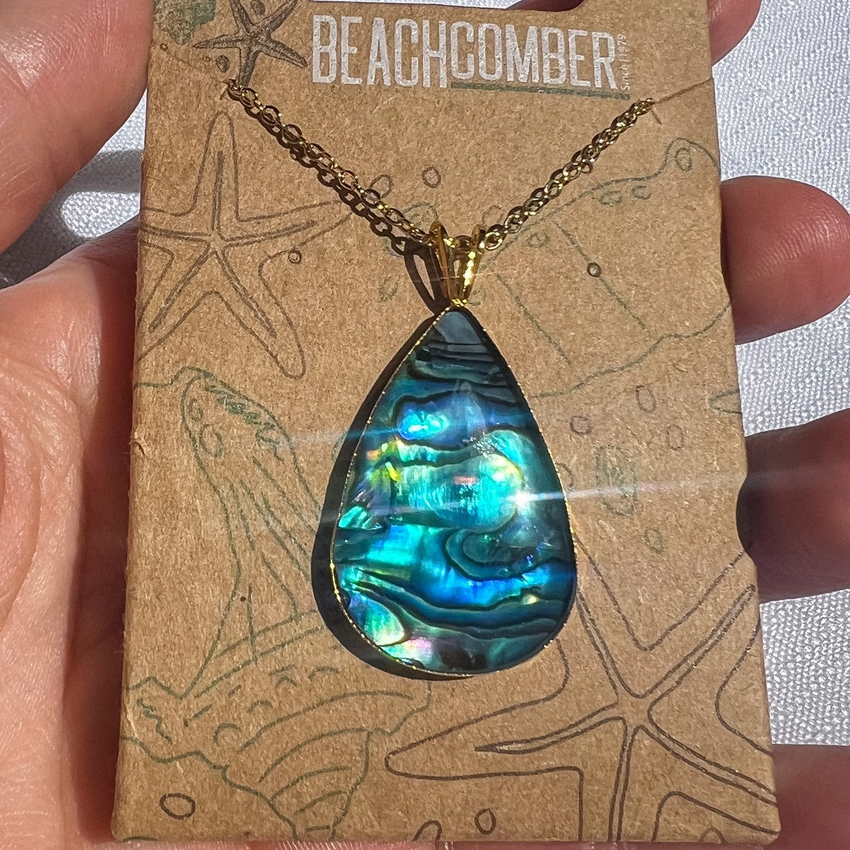 Necklace with a teardrop-shaped abalone shell pendant on a 'Beachcomber' branded card.