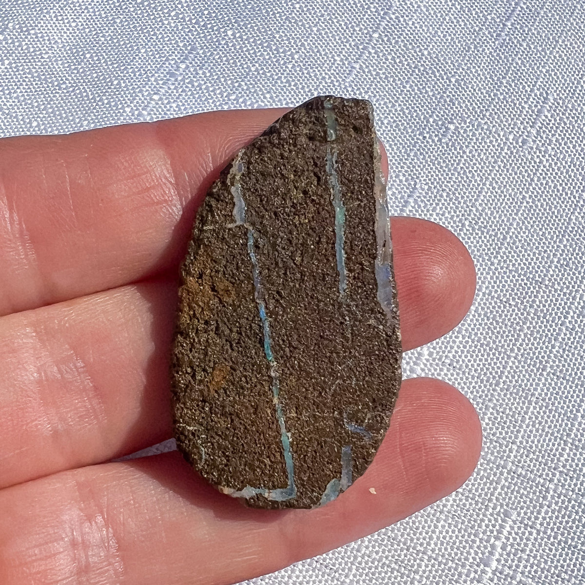 Queensland boulder opal rough specimen with brown tones and narrow pale blue-green seams, measuring 40 × 23 × 5 mm
