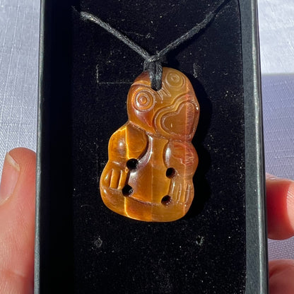 Carved stone pendant on a black background held by a hand