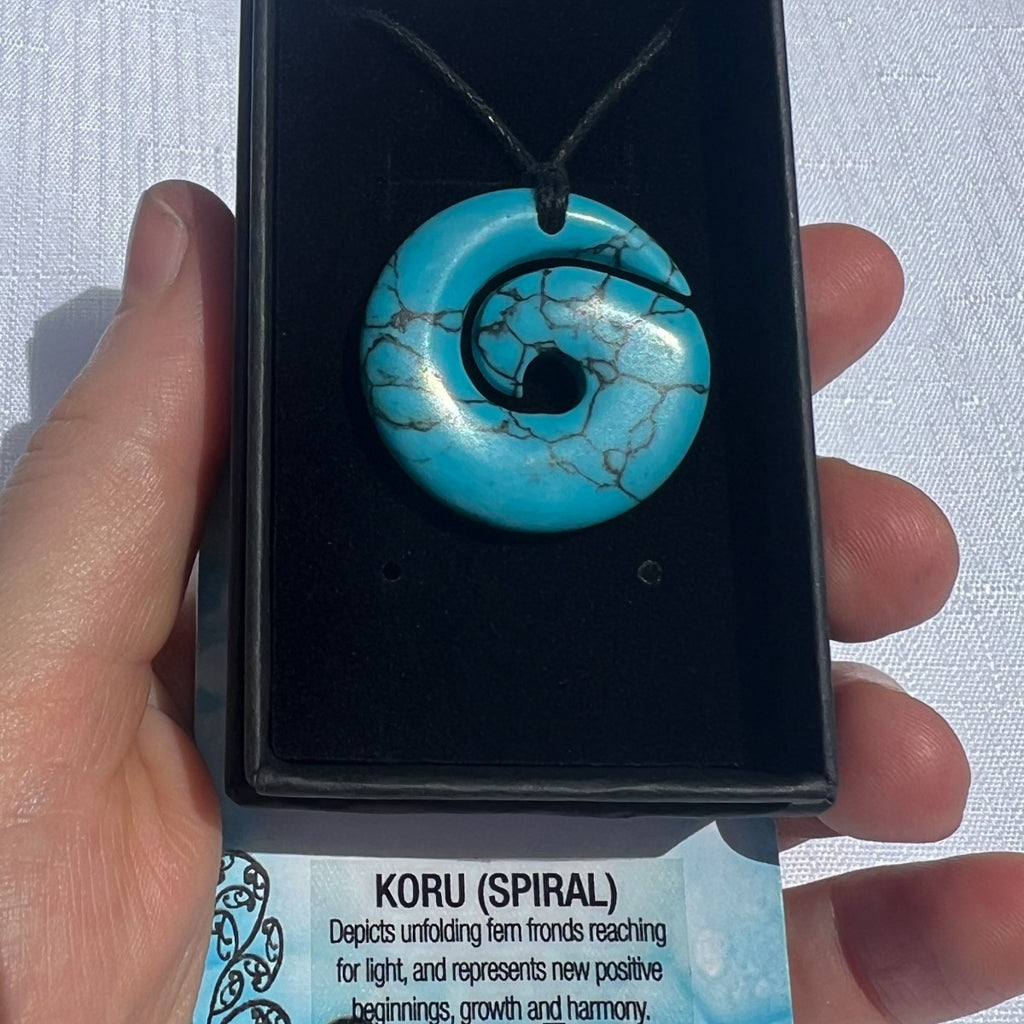 Turquoise koru pendant on a black card held by a hand with a white background
