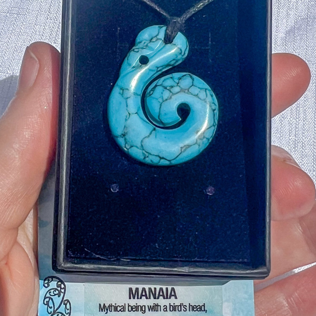 Turquoise spiral pendant on a card held by a hand