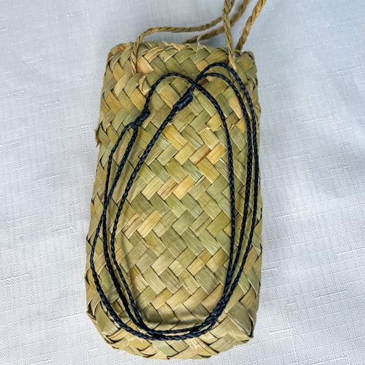 Braided black slip knot cord for greenstone pendant, displayed neatly coiled on top of a traditional woven flax kete bag.