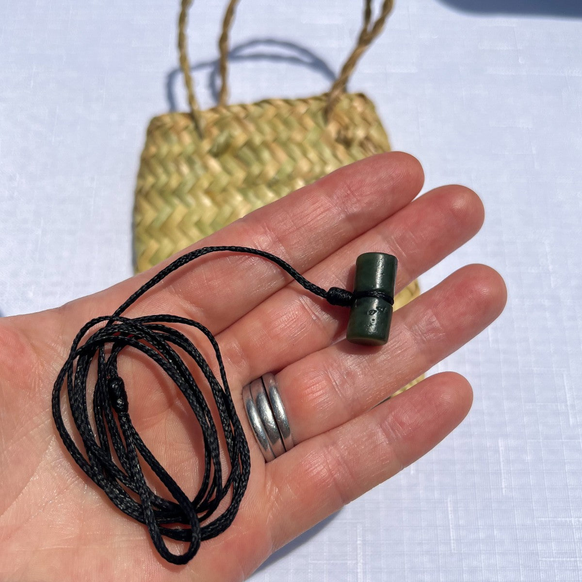 Hand holding a greenstone barrel toggle on a fixed black waxed cord, suitable for New Zealand greenstone pendants.