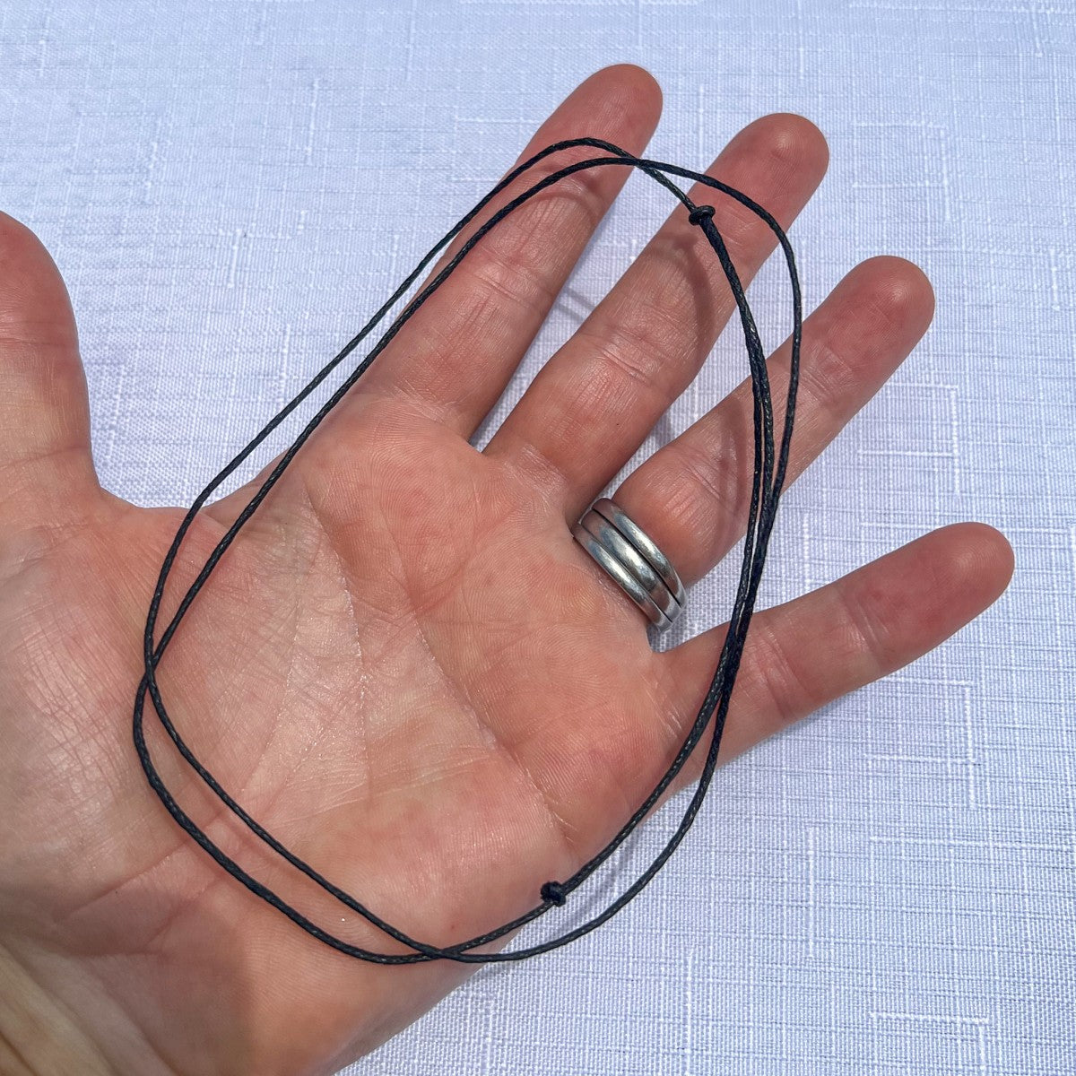 Hand holding a black adjustable slipknot cord for New Zealand greenstone pendants, shown against a white background.