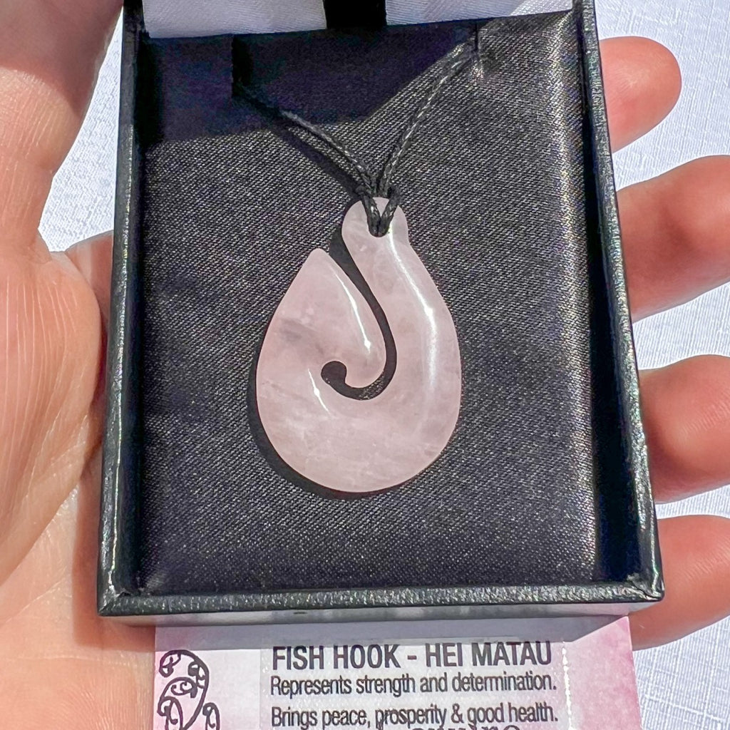Rose quartz Hei Matau (fish hook) pendant necklace on a black cord, symbolising love, strength, and safe travel — hand-carved in New Zealand.