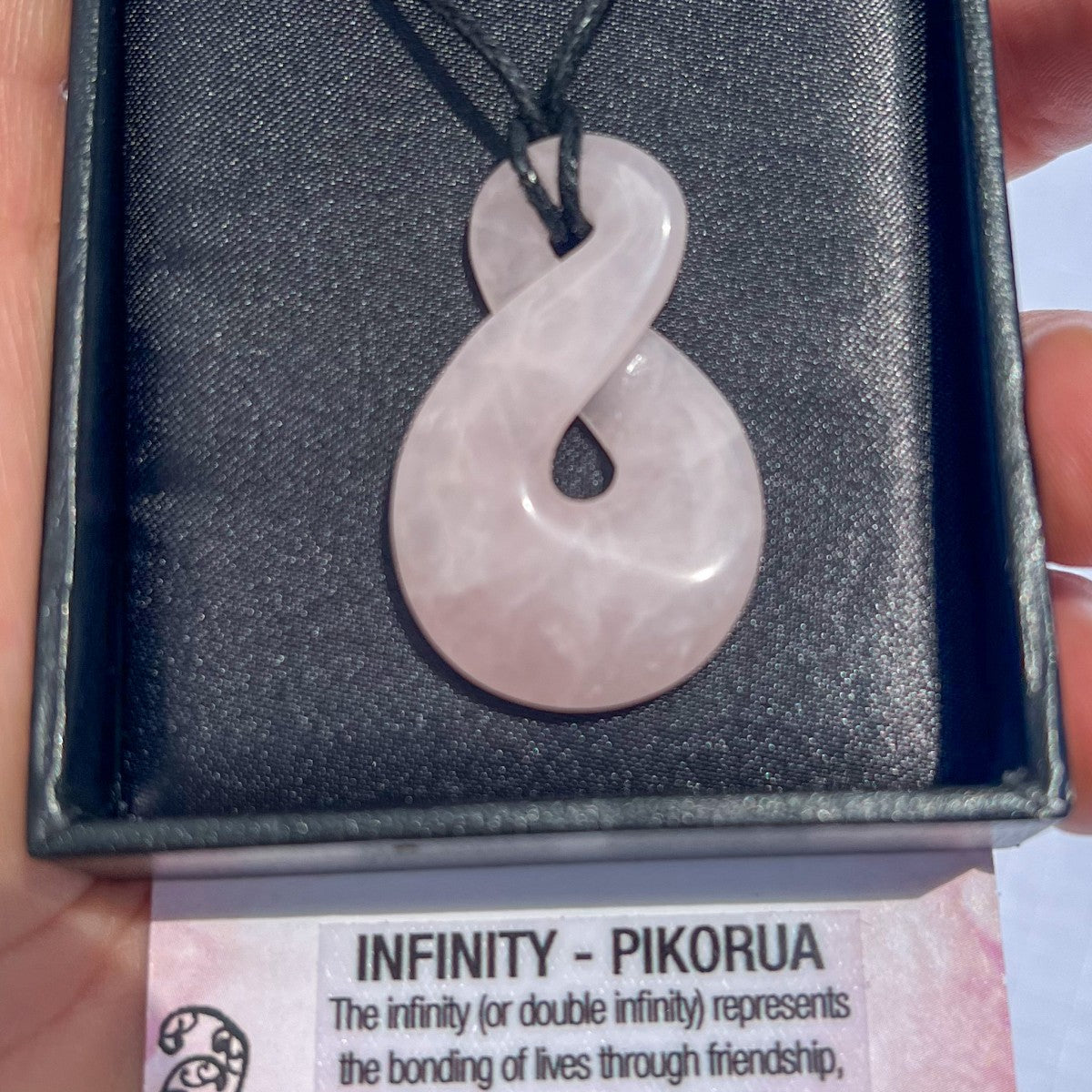 Rose quartz Pikorua (infinity twist) pendant necklace on a black cord, symbolising eternal love, friendship, and connection — hand-carved in New Zealand.