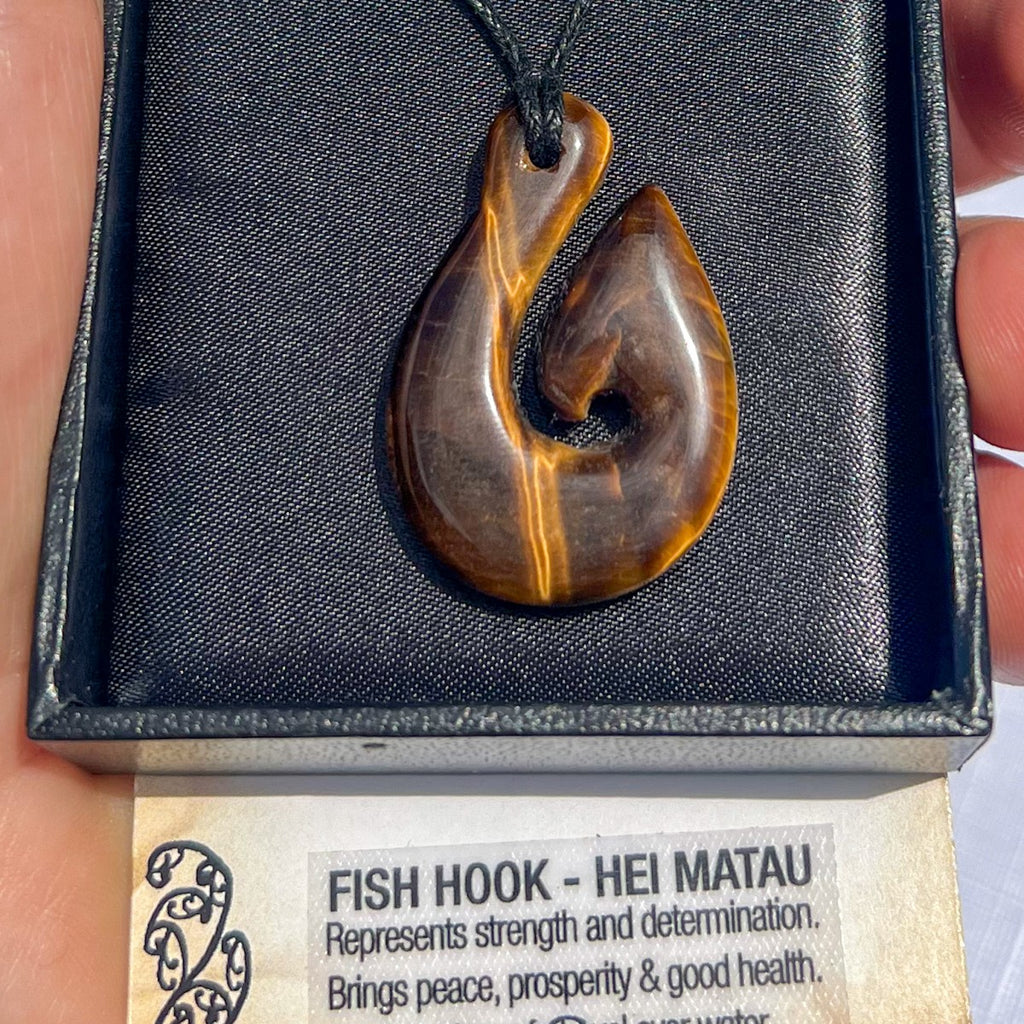 Tiger eye Hei Matau (fish hook) pendant necklace on a black cord, symbolising strength, prosperity, and safe passage — hand-carved in New Zealand.