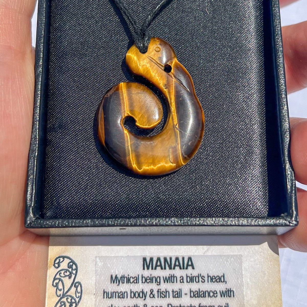 Tiger eye Manaia pendant necklace on a black cord, symbolising spiritual protection and balance — hand-carved in New Zealand with golden-brown stone.