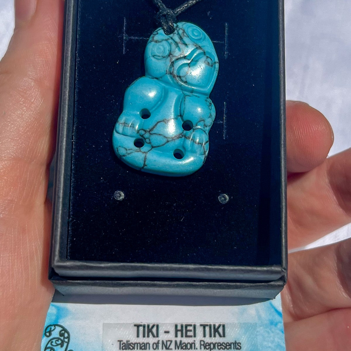 Turquoise tiki pendant in a display case held by a hand